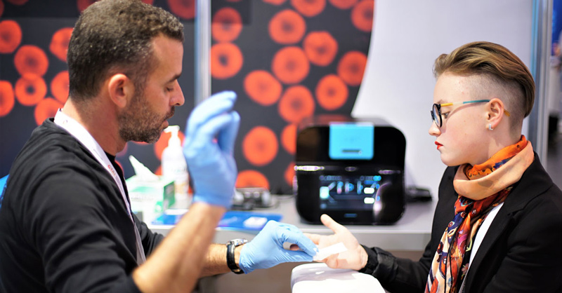 A lab tech performs a simple blood test on a patient. The OLO machine is in the background.