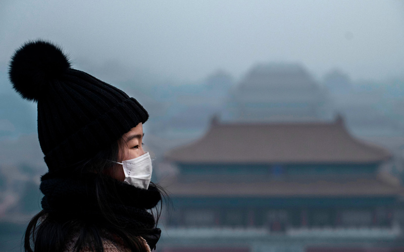 A woman wears a protective mask on January 26 as she stands on an overlook near Beijing’s Forbidden City.