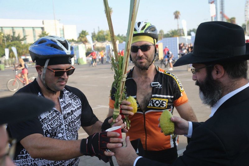 Cyclists in Tel Aviv pause to holds the four species – palm branch, etrog, myrtle and willow – before bicycle race in Tel Aviv during Sukkot 2016.